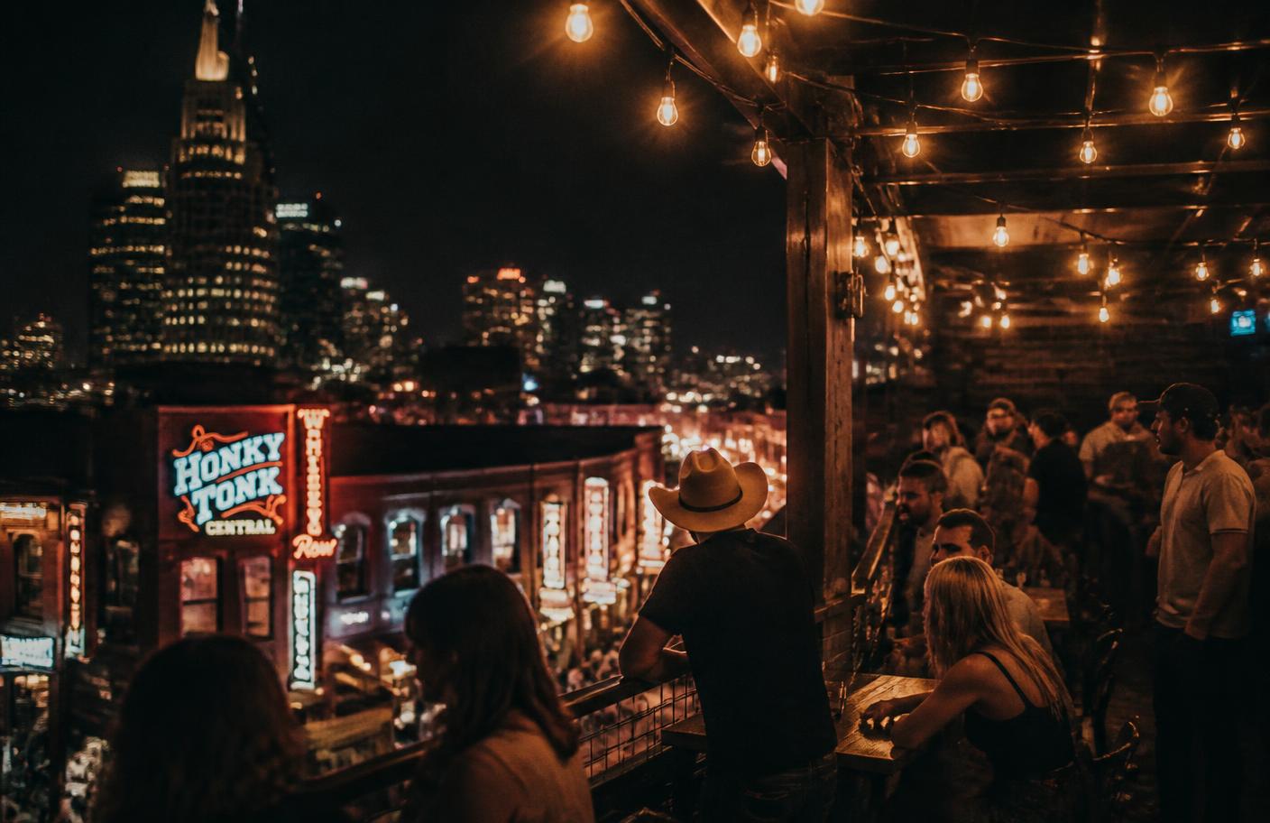 String lights over a Lower Broadway rooftop with the Nashville skyline behind